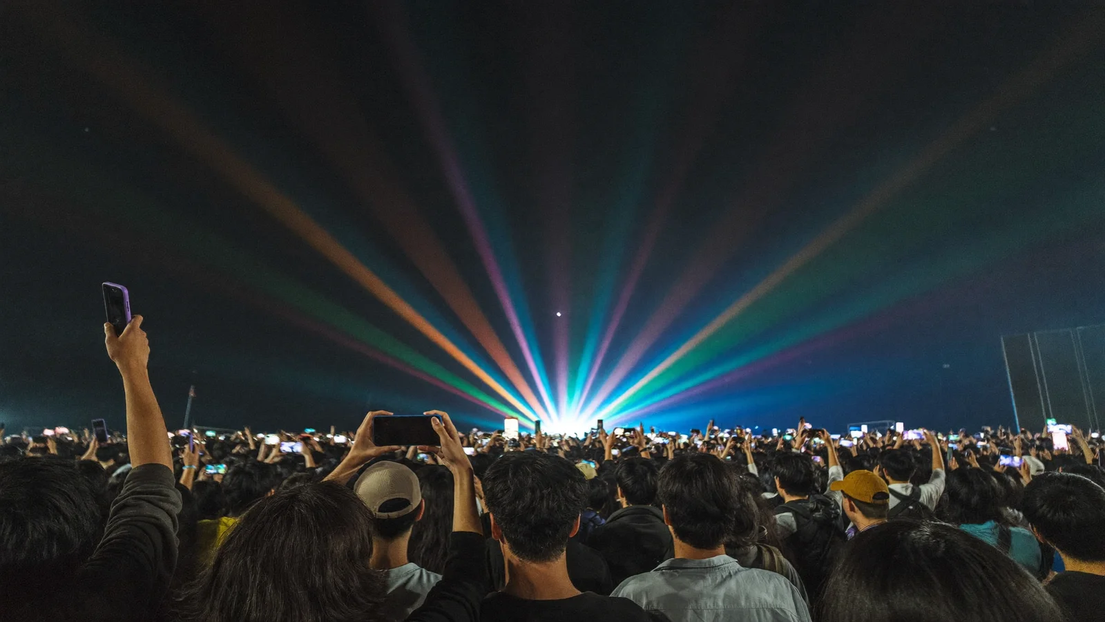 Illustrative image of a stadium crowd holding up phones as coloured light beams sweep the stage