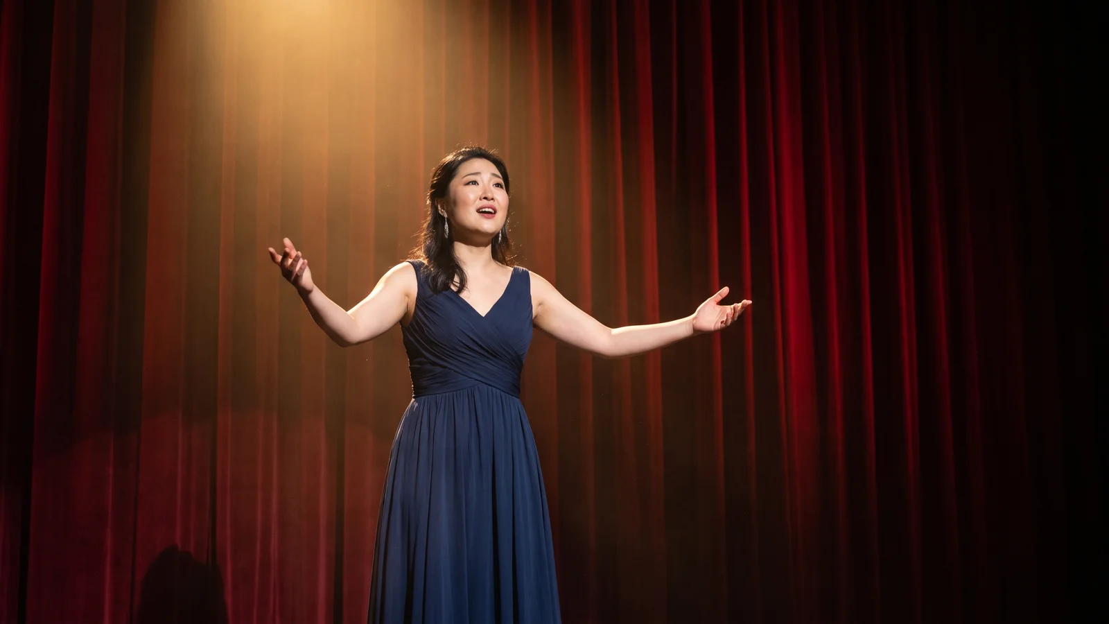 Illustrative image of a dramatically lit opera stage with a lone performer against a deep red curtain, not a photo of the Opera Hong Kong production