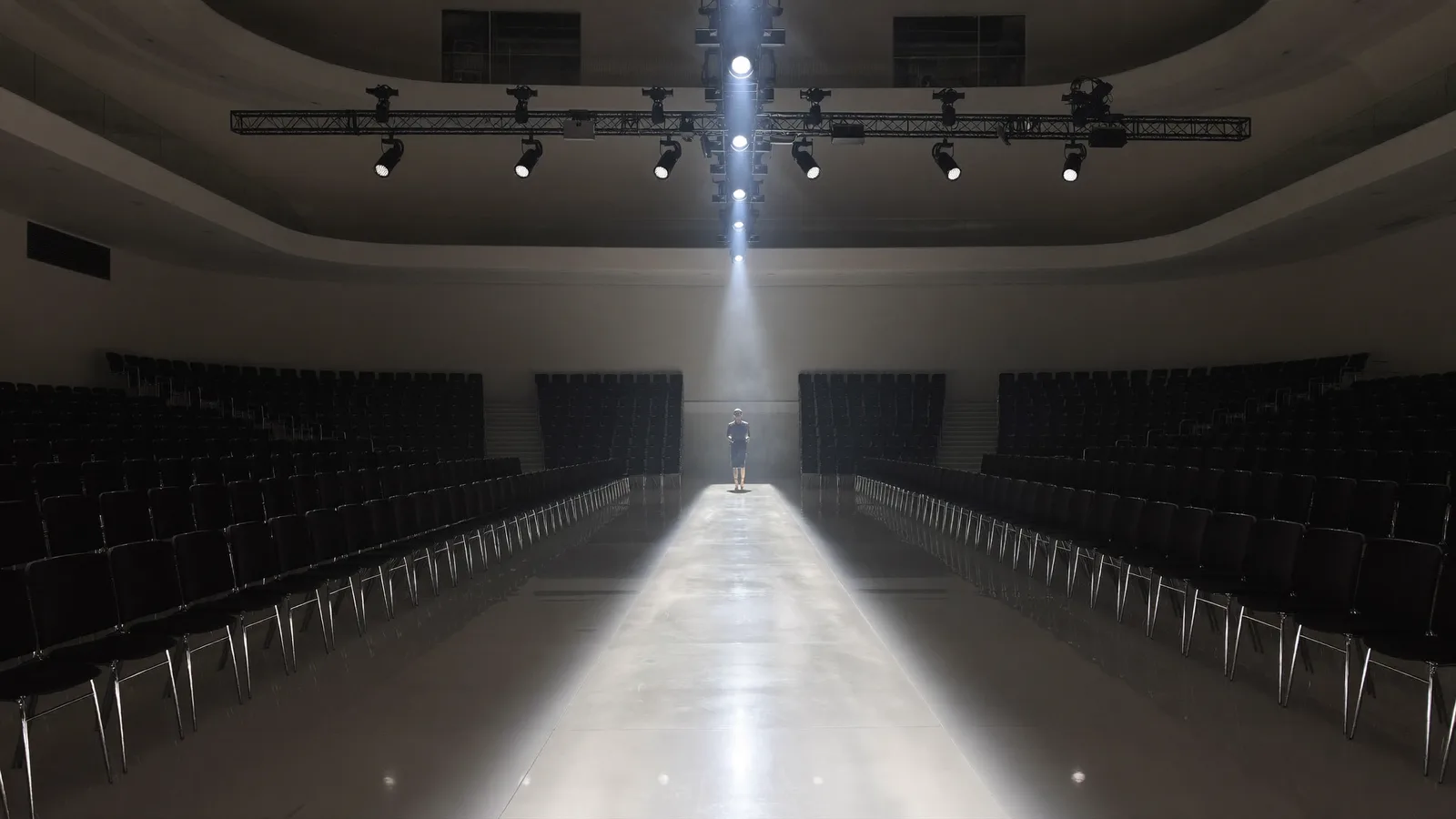 A wide atmospheric empty fashion runway inside a convention hall with rows of empty audience chairs, illustrative hero for CENTRESTAGE 2026 at HKCEC
