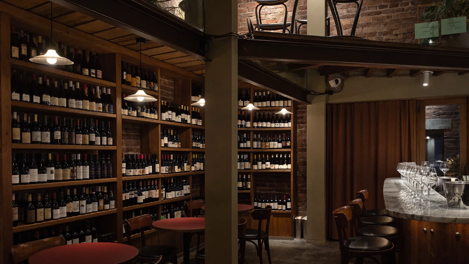 A warmly lit two-storey wine bar interior with wooden wine racks and a marble counter, illustrative hero for James Suckling Wine Central's new Shin Hing Street home