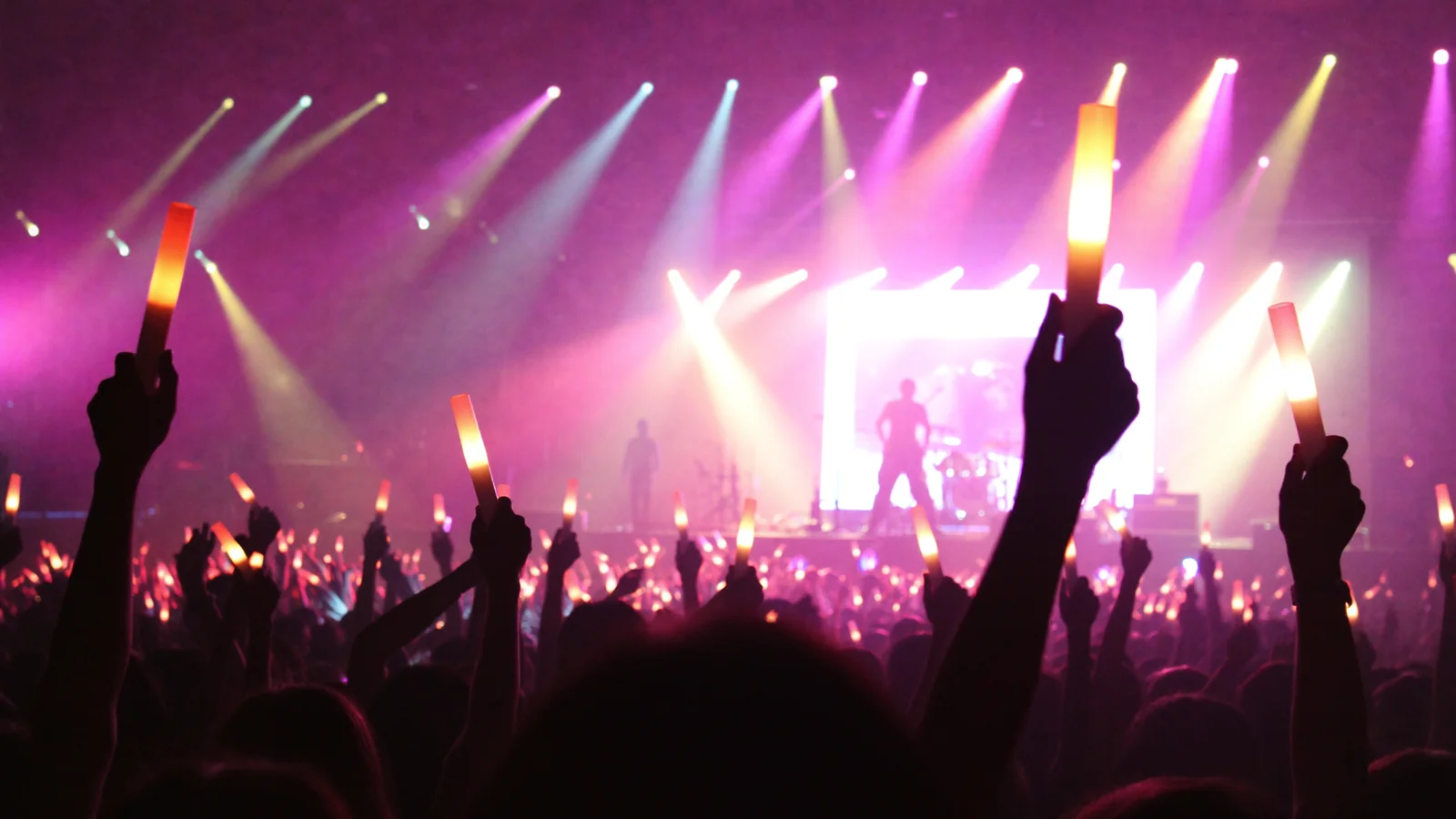 A concert crowd raising glowing light sticks toward a brightly lit arena stage, illustrating Lee Youngji's Hong Kong show