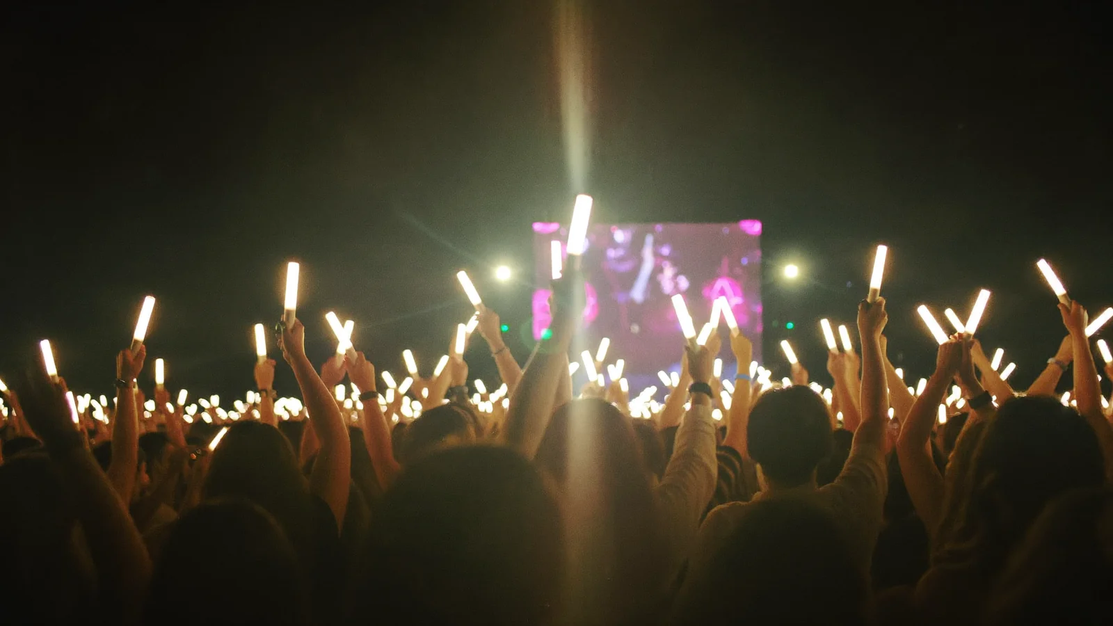 Illustrative image of a K-pop arena stage with sweeping coloured lights over a standing crowd