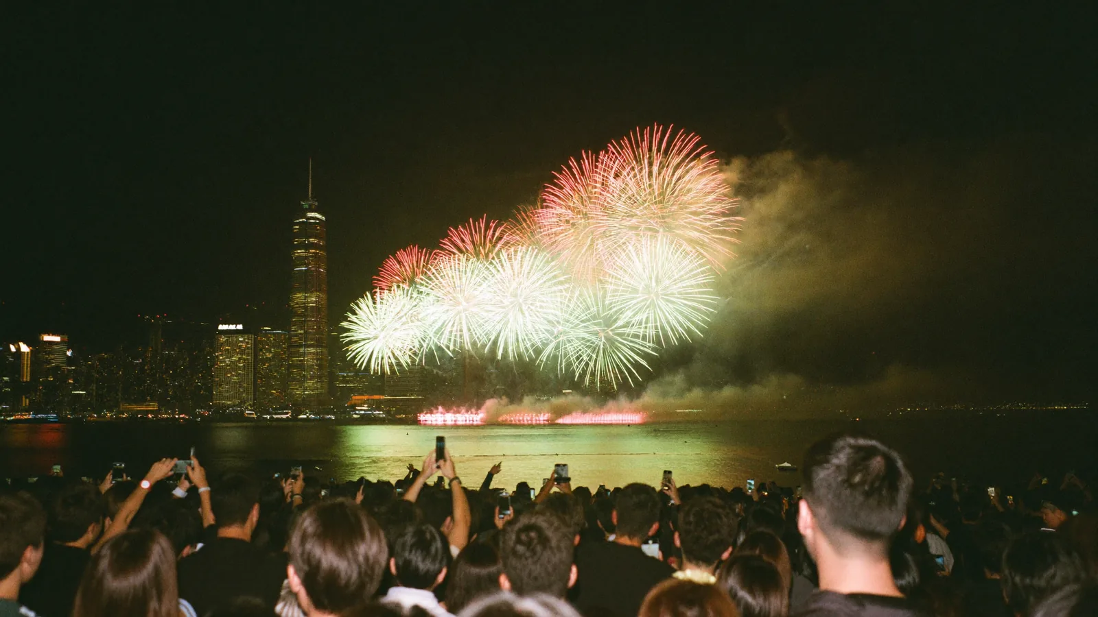 Illustrative image of a harbourfront crowd watching fireworks burst over Victoria Harbour at night