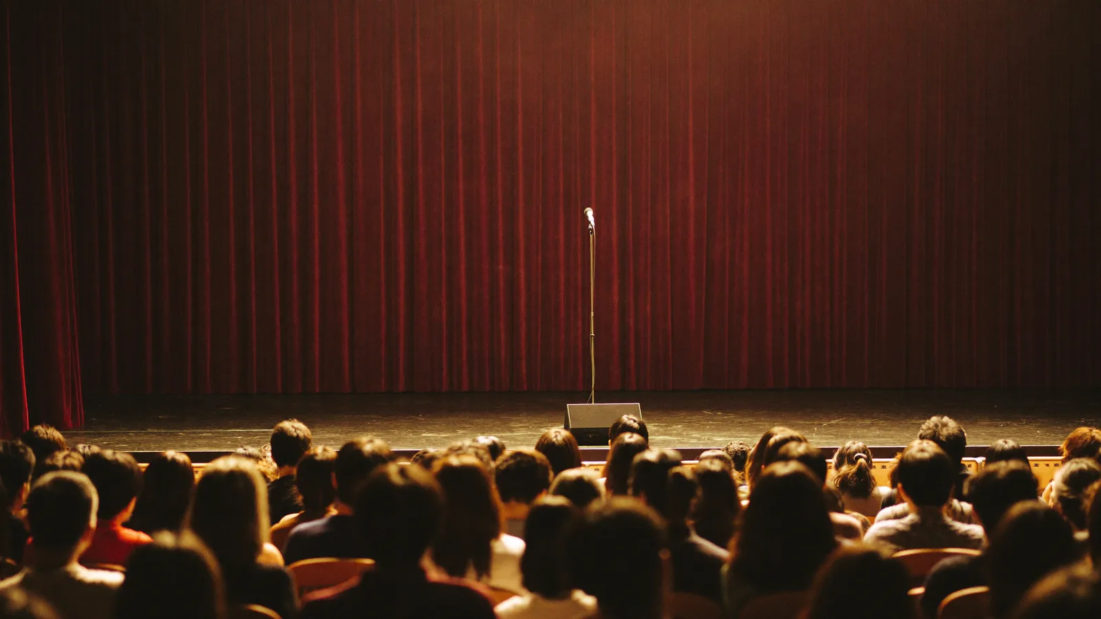 Illustrative image of a stand-up comedy stage with a single microphone in front of a seated audience